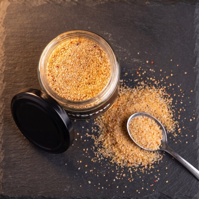 An open jar of Inferno with salt spilled across slate and a spoon